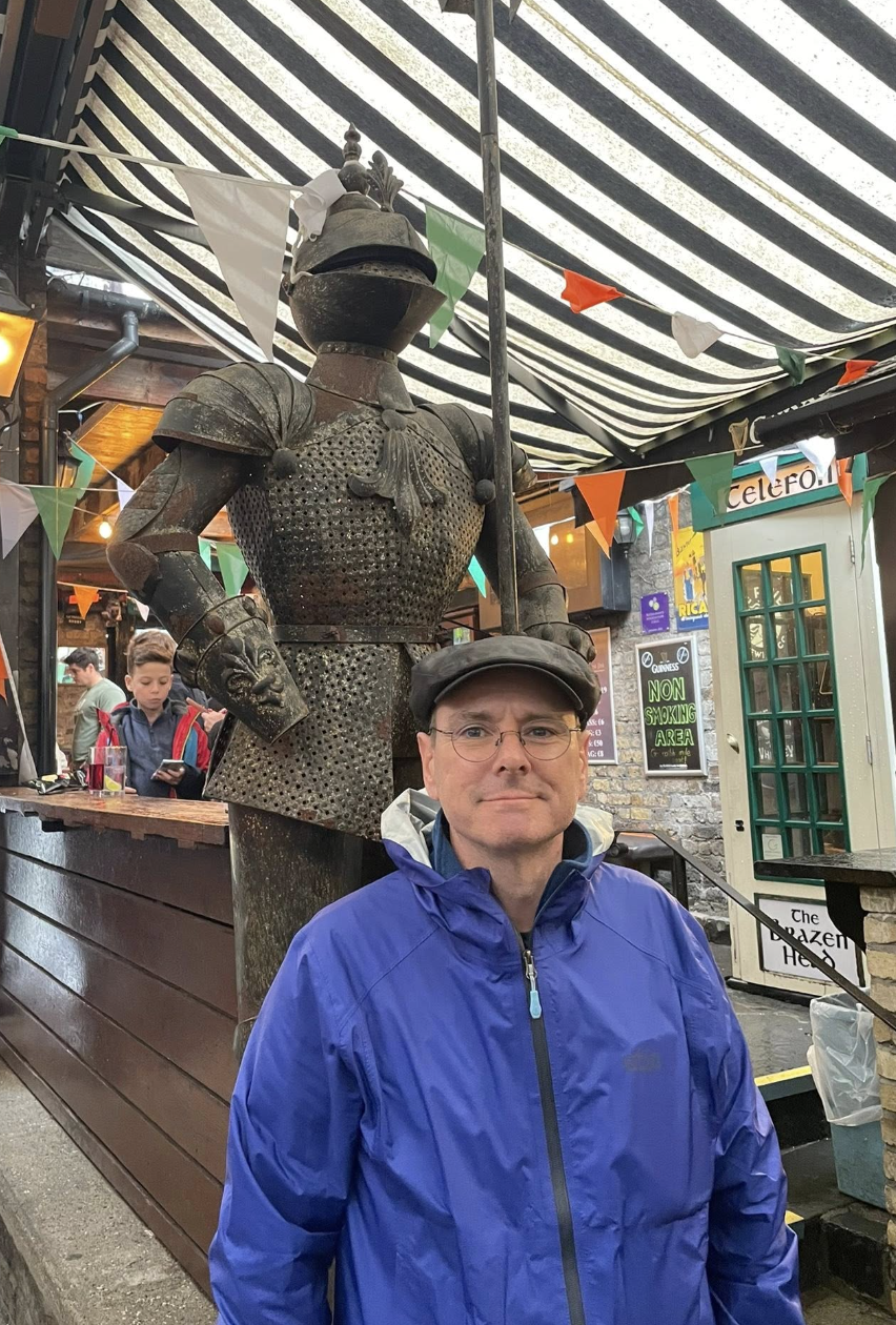 man stands smiling infront of knight statue