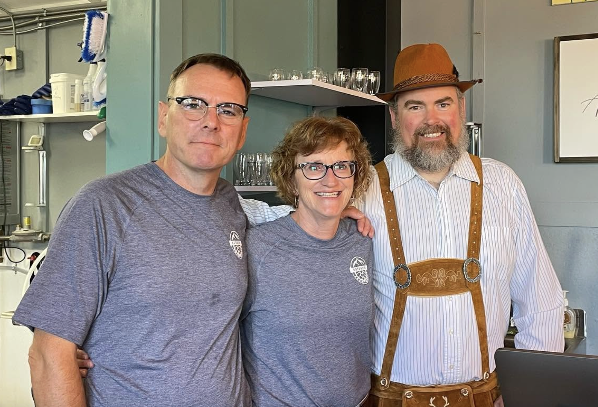 Three people arm in arm smiling for a photo (one is in lederhosen)